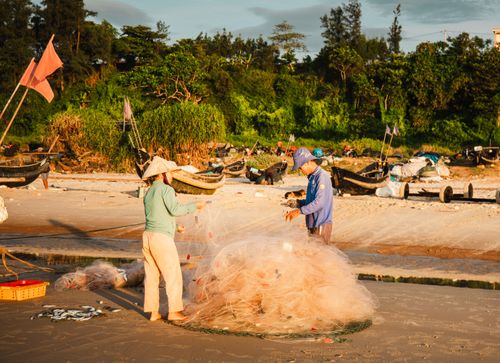 Free Two fishermen working with nets on a beach in Quảng Trị, Vietnam, during sunset. Stock Photo