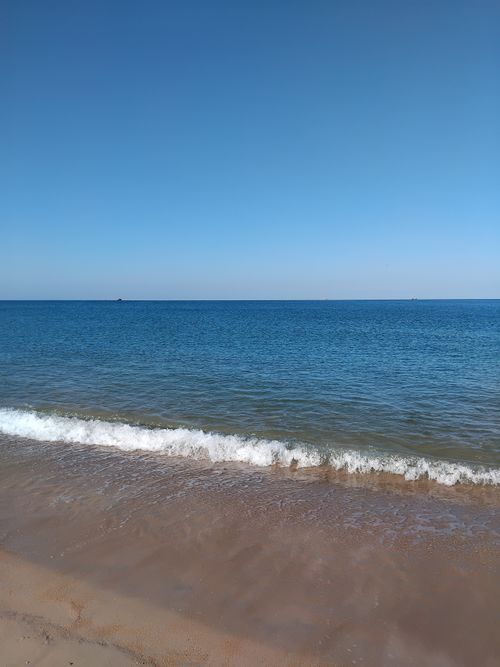 Free Peaceful seascape with gentle waves on a sandy beach under a bright blue sky. Stock Photo