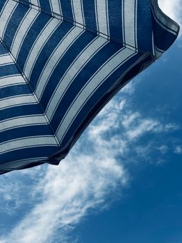 A blue and white striped umbrella with a clear sky and wispy clouds.