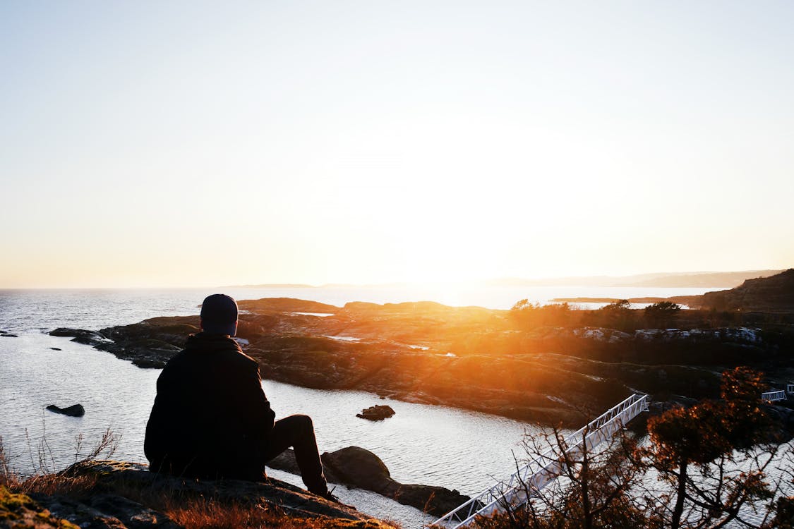 Silhouette Photo of Person Sitting Near Cliff during Golden Hour 