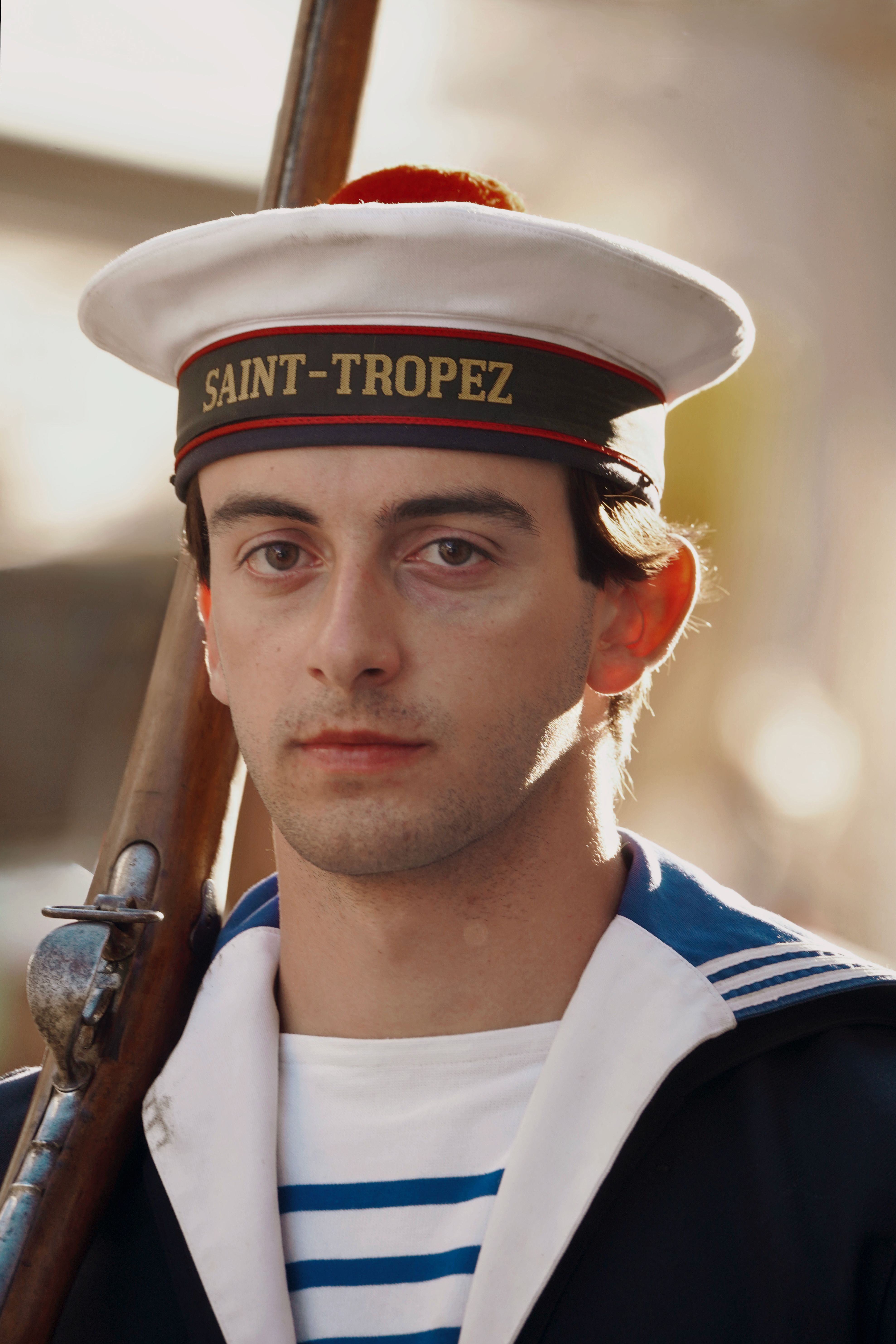 Portrait of a sailor in a vintage Saint-Tropez uniform, holding a rifle.