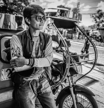 A young man poses with a tricycle in a street scene, Philippines.