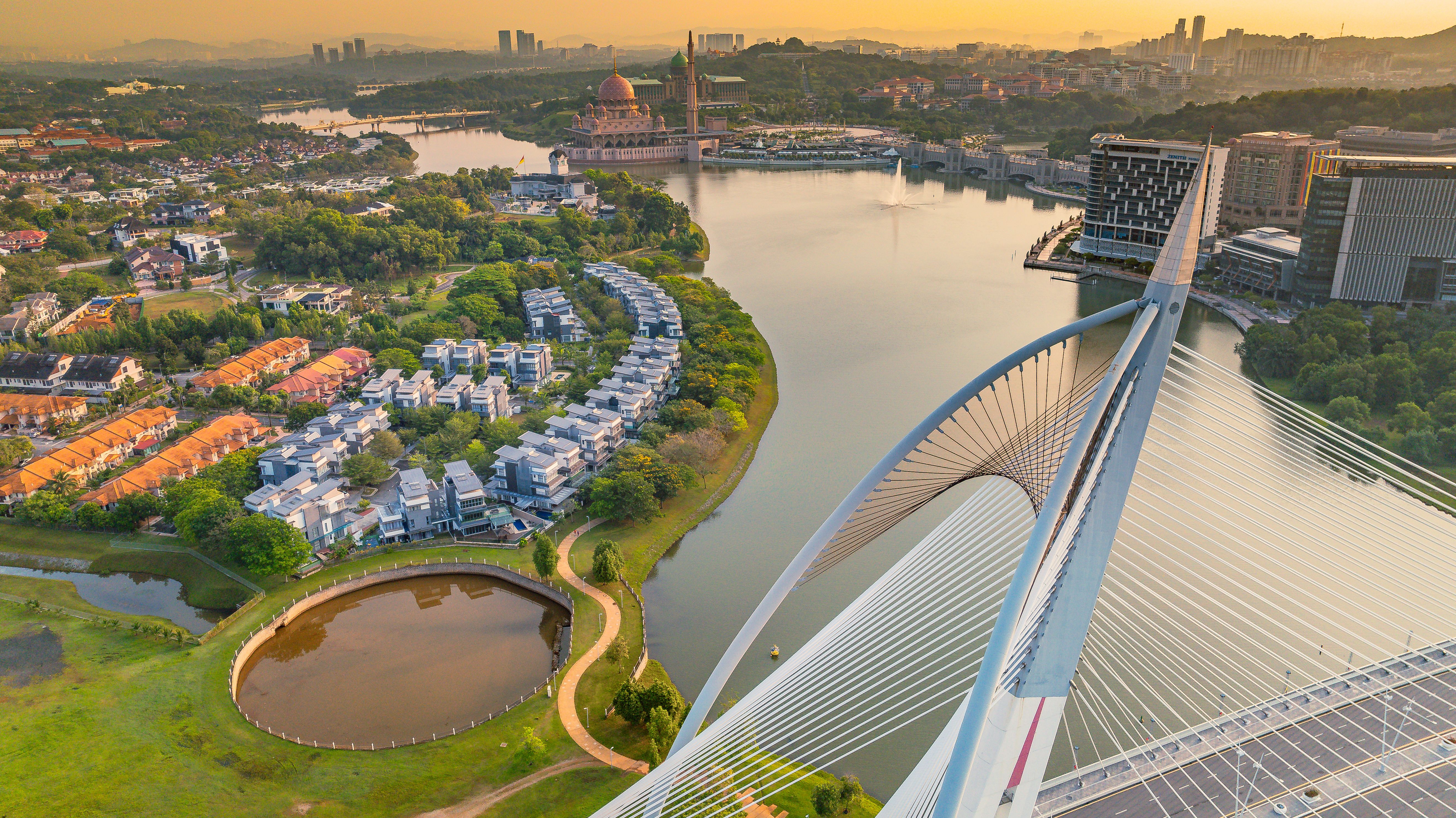 Stunning aerial view of Putrajaya featuring iconic bridge and city skyline at sunset, highlighting urban beauty.