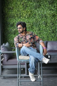 Man wearing sunglasses and casual attire relaxing on a chair indoors.