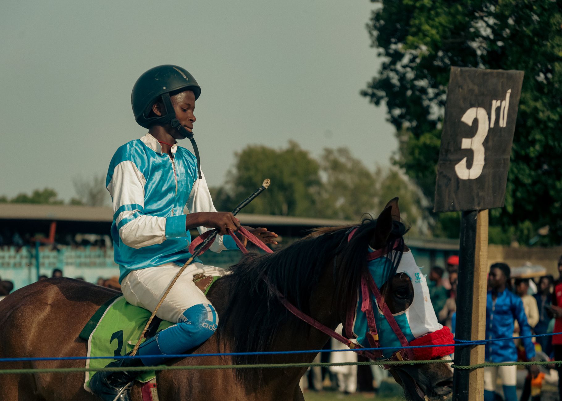 A young equestrian competing in a horse race, finishing in third place, under a clear sky.