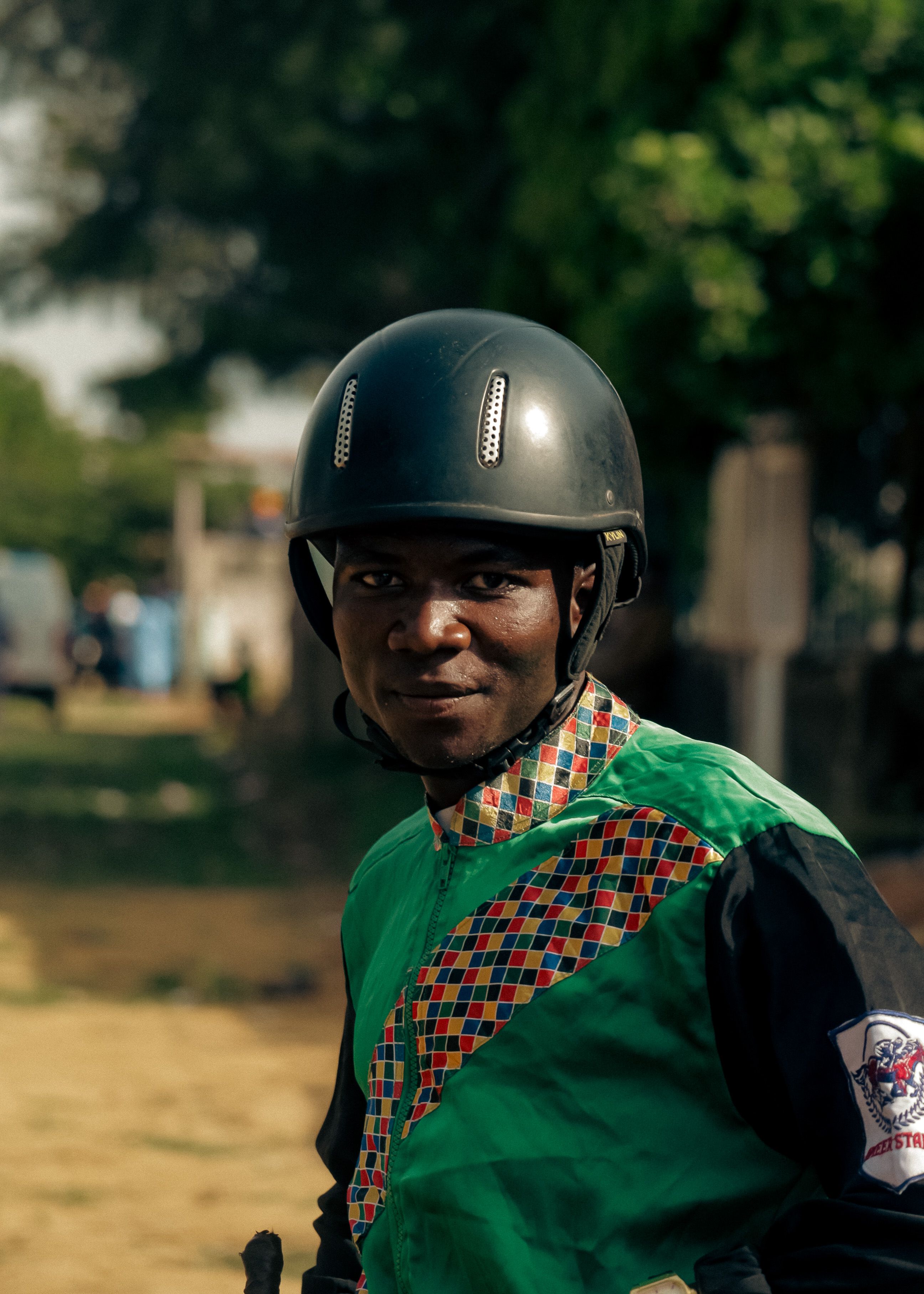Smiling motorcyclist wearing colorful traditional attire and helmet outdoors.