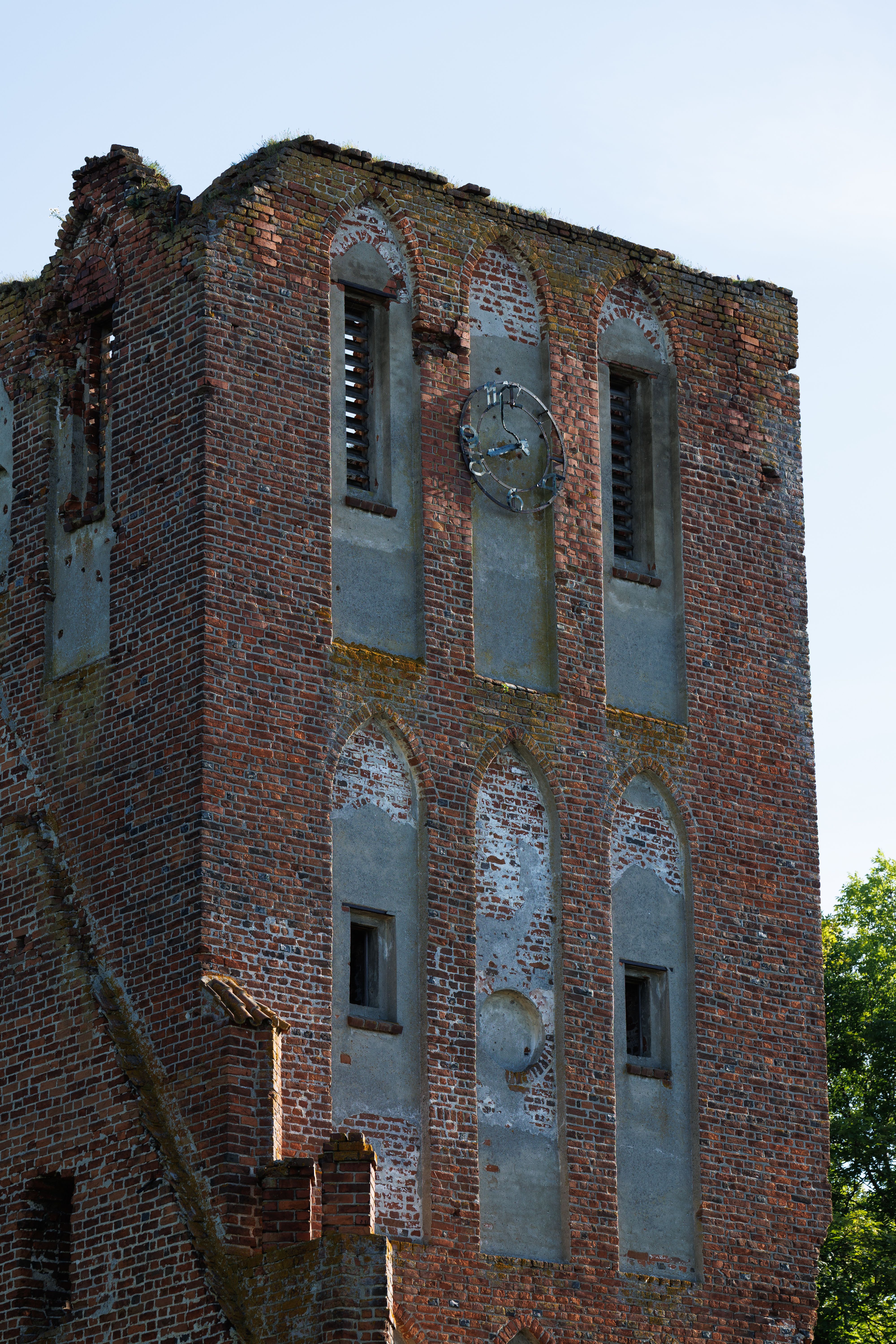 A weathered brick tower with arched windows and clock, set against a clear blue sky.