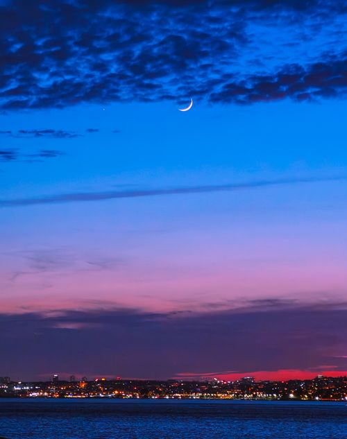 Free A stunning view of a crescent moon above a cityscape with vibrant twilight colors. Stock Photo