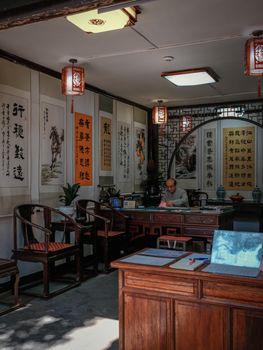 Authentic interior of a traditional Chinese calligraphy studio with decorative scrolls, lanterns, and a calligrapher at work.