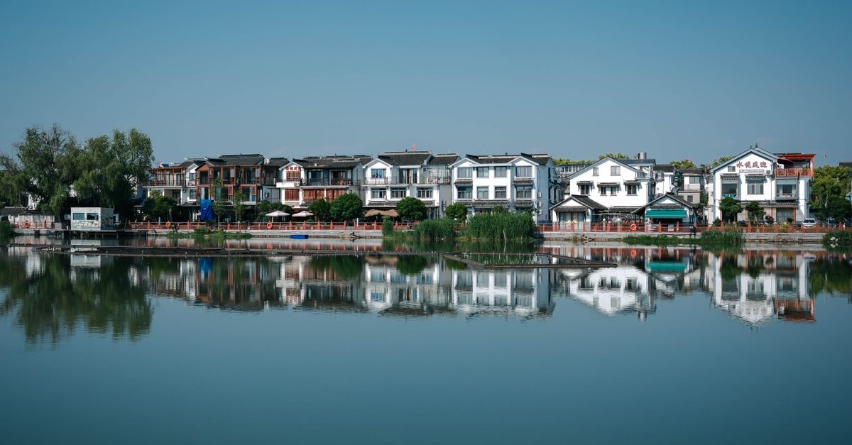 Charming traditional homes reflecting in calm lake waters under a clear blue sky.