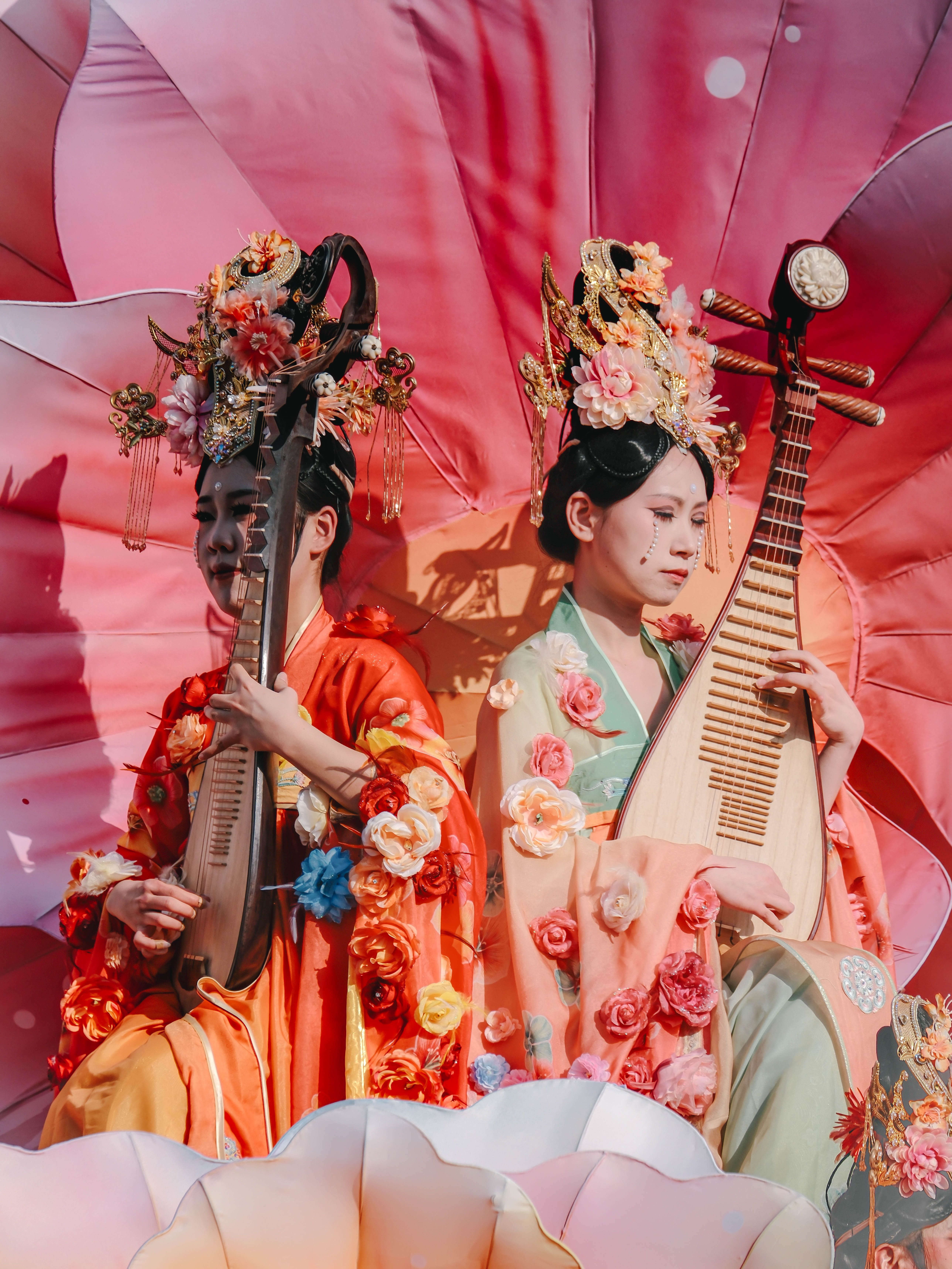 Two Chinese women in vibrant traditional costumes playing musical instruments.