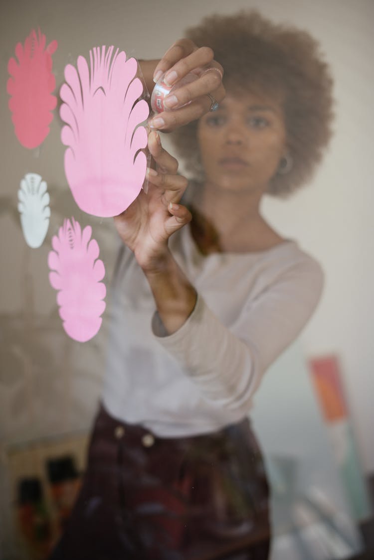 Concentrated Black Female Artisan Sticking Paper Flowers On Glass Wall