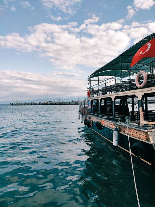 Free A scenic view of a traditional Turkish boat docked at Sinop harbor under a partly cloudy sky. Stock Photo