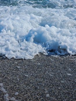 Detailed image of ocean waves creating sea foam on a sandy beach.