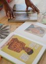 From above of crop female artist examining pictures in books of art and standing at table in contemporary flat