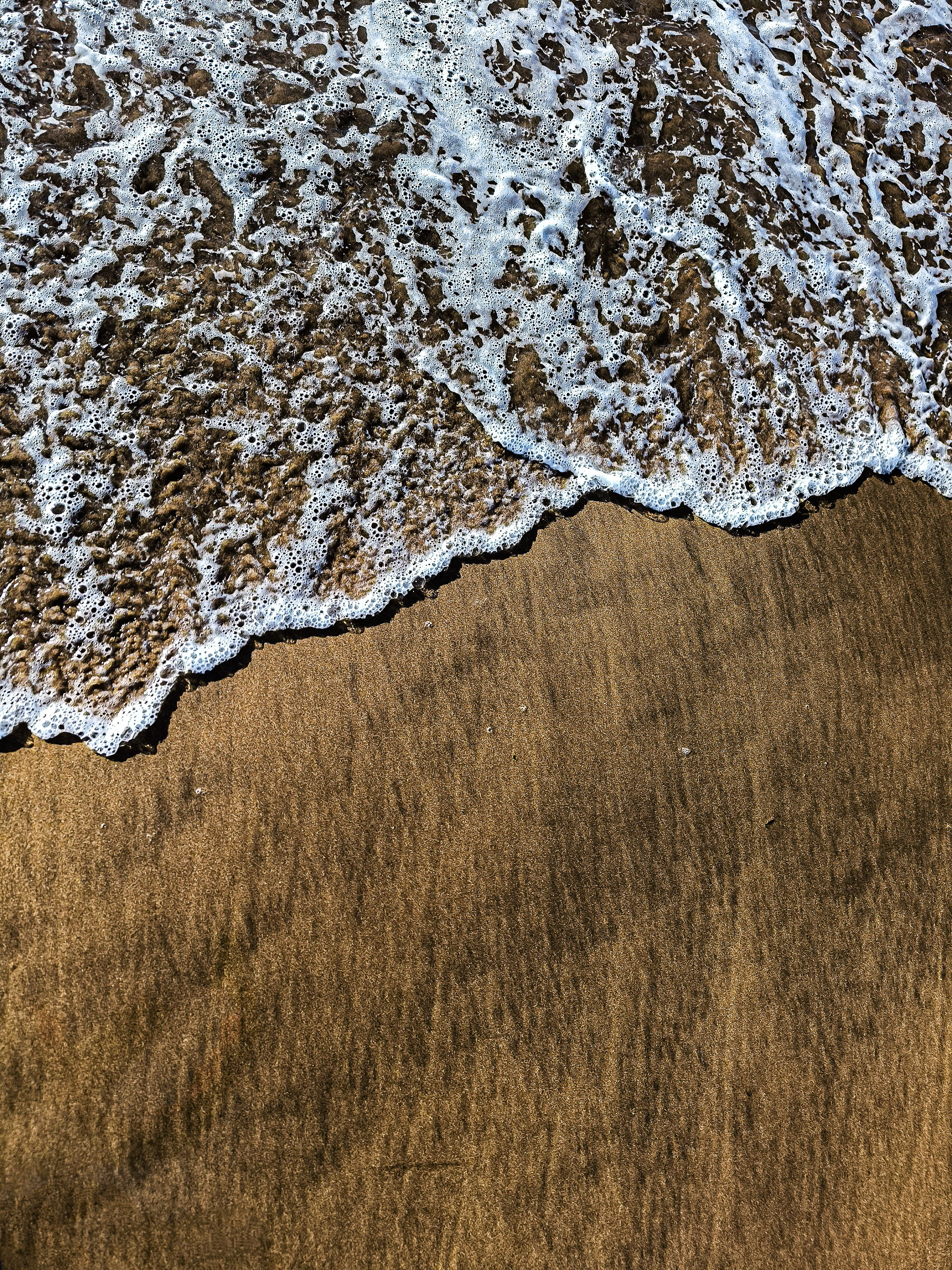 Close-up of foamy ocean waves washing over a golden sandy beach, capturing a serene coastal moment.