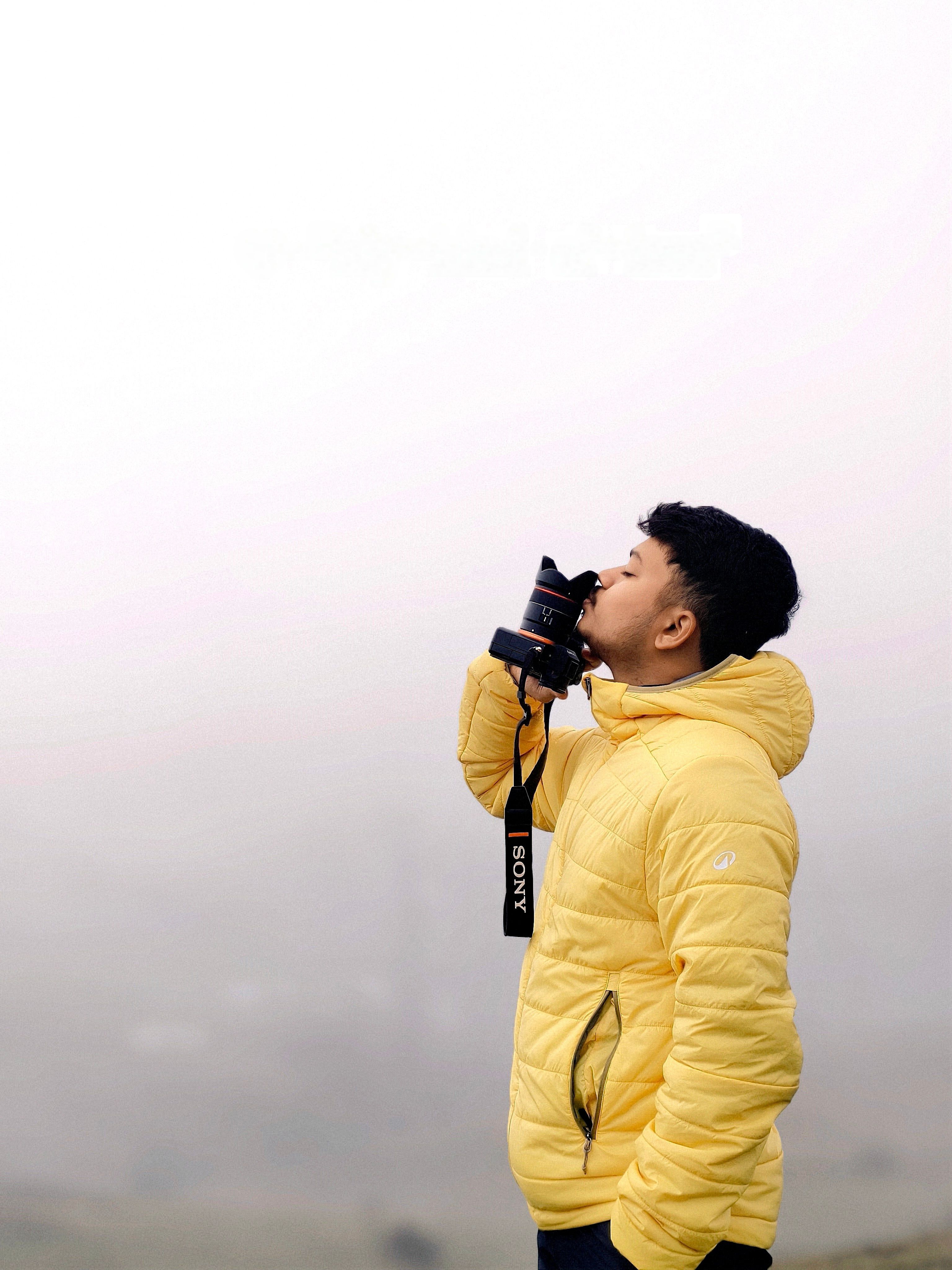 A man in a yellow jacket enjoys misty weather, holding a camera.