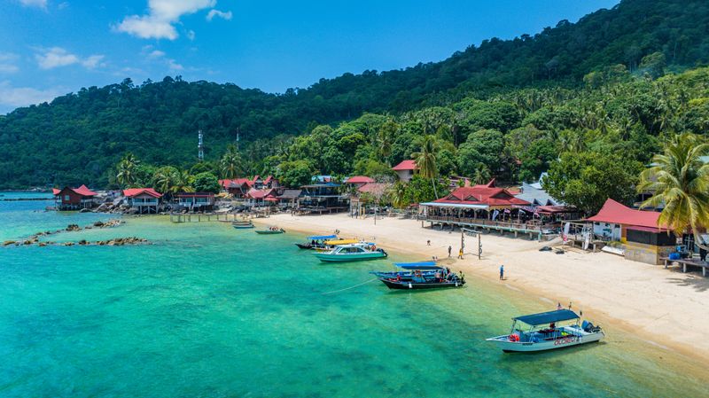 Stunning aerial view of Tioman Island's beach, Pahang, Malaysia, showcasing turquoise waters, boats, and lush greenery.
