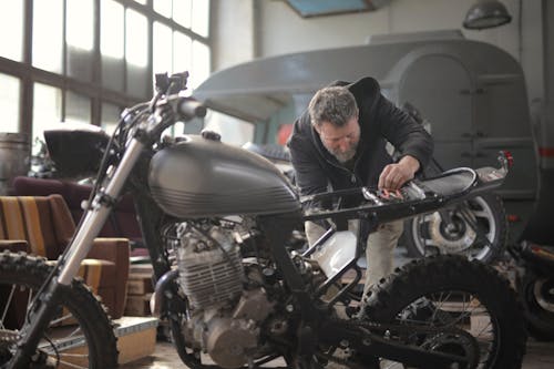 免費 穿黑夾克的男人站在黑色的摩托車附近 圖庫相片