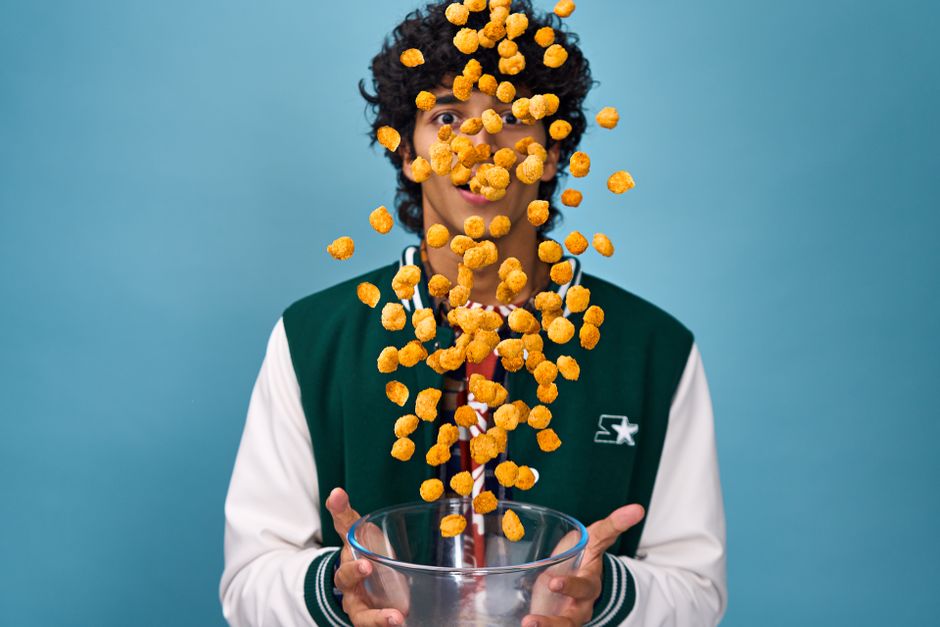 A young adult playfully tosses cereal puffs into the air, creating a dynamic portrait.