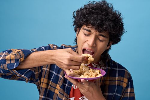 Free A young man eagerly eating Indian bread and curry against a blue background. Stock Photo