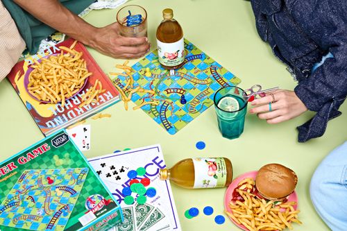 Free Young adults enjoy a casual game night with snacks, soda, and board games on a vibrant table. Stock Photo