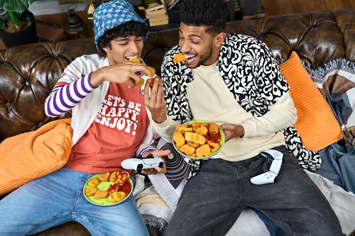 Free Two friends eating snacks and playing games on a comfortable leather couch, enjoying leisure time. Stock Photo