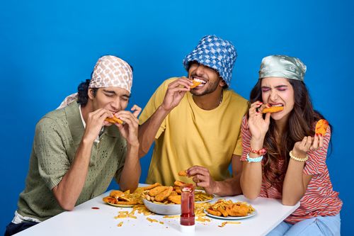 Free Three friends having fun eating fried snacks, showcasing friendship and enjoyment. Stock Photo