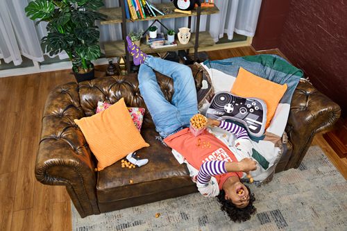 Free A young adult lying upside down on a sofa, having fun while snacking indoors. Stock Photo