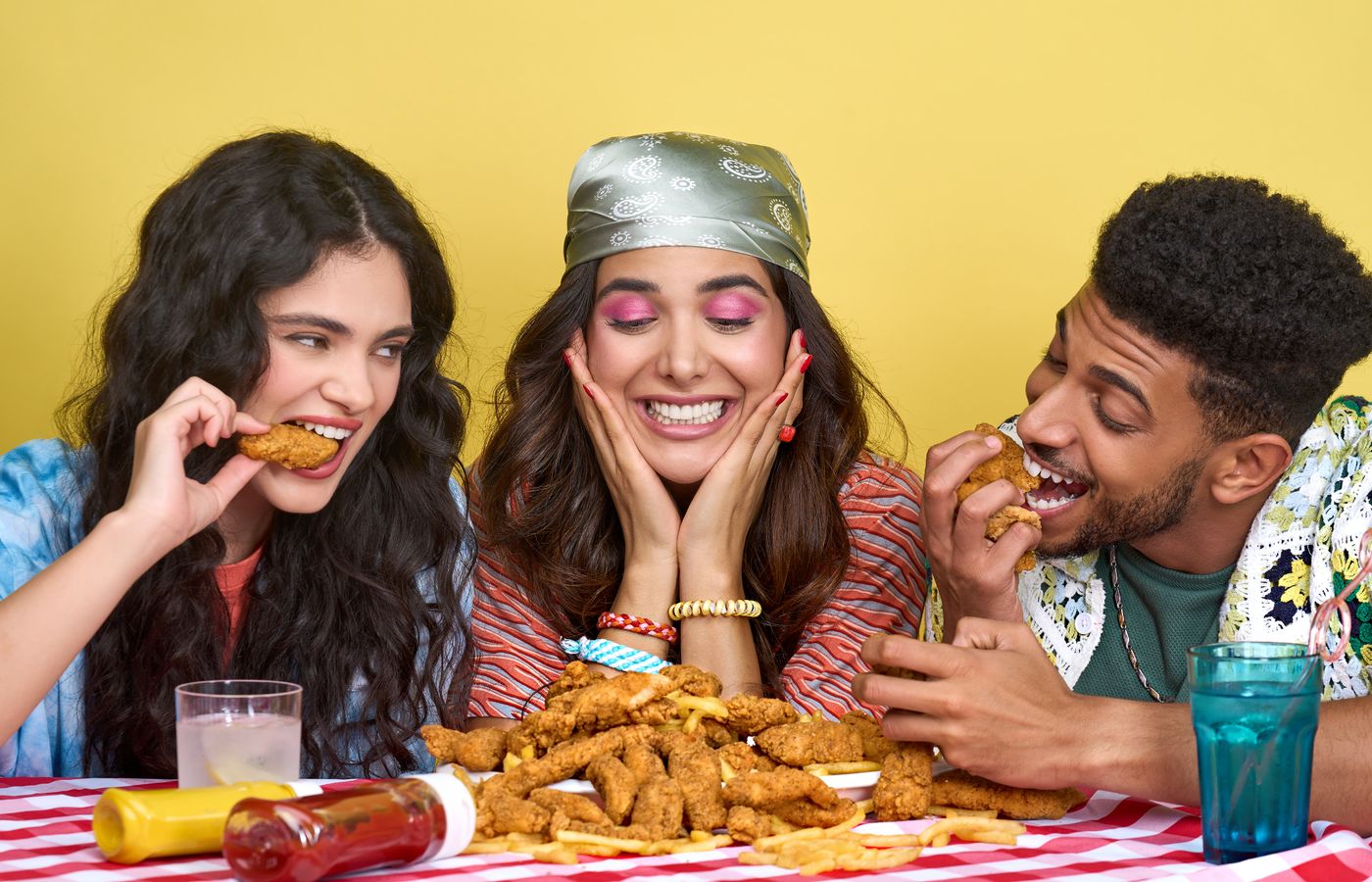 Three friends indulge in a joyful fried chicken meal at a colorful table setting.