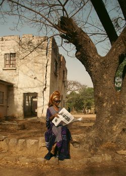 African woman in traditional attire reading a newspaper outdoors near an old building