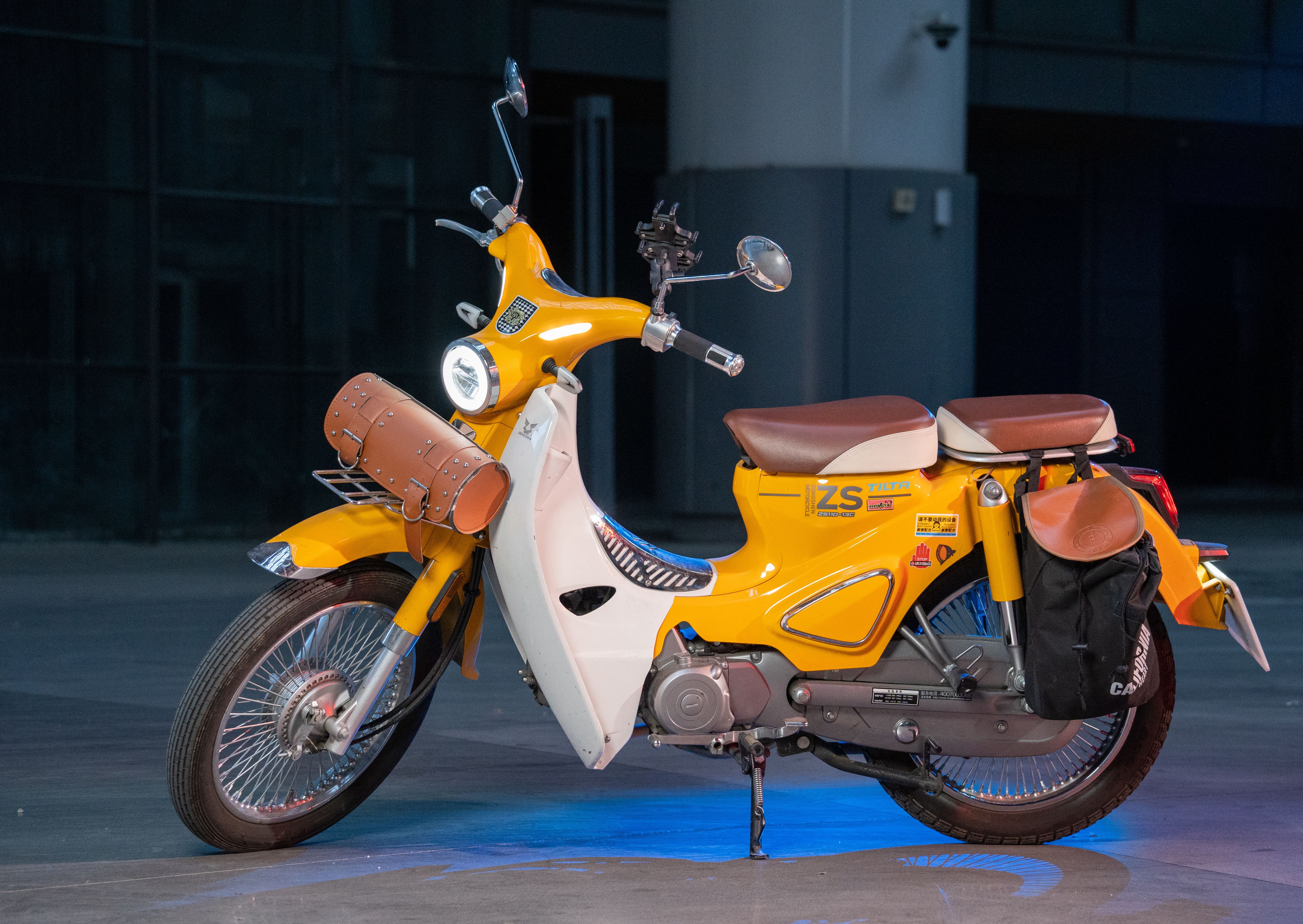 Yellow retro scooter with a saddlebag parked on an urban street at night.