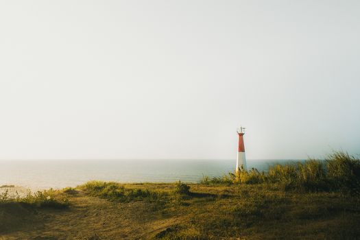 A peaceful seaside scene with a solitary lighthouse surrounded by grassy landscape at sunset.