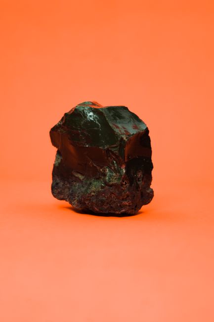 Close-up of a glossy obsidian rock showcased on a vibrant orange background, highlighting its natural texture. - Overview of Shilajit and Its Origins