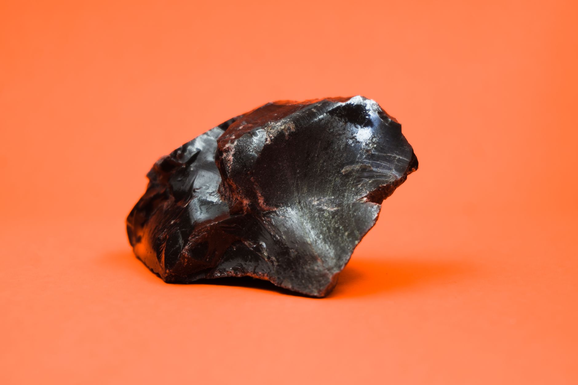 Close-up shot of a glossy obsidian stone with a sharp texture against a vibrant orange background.