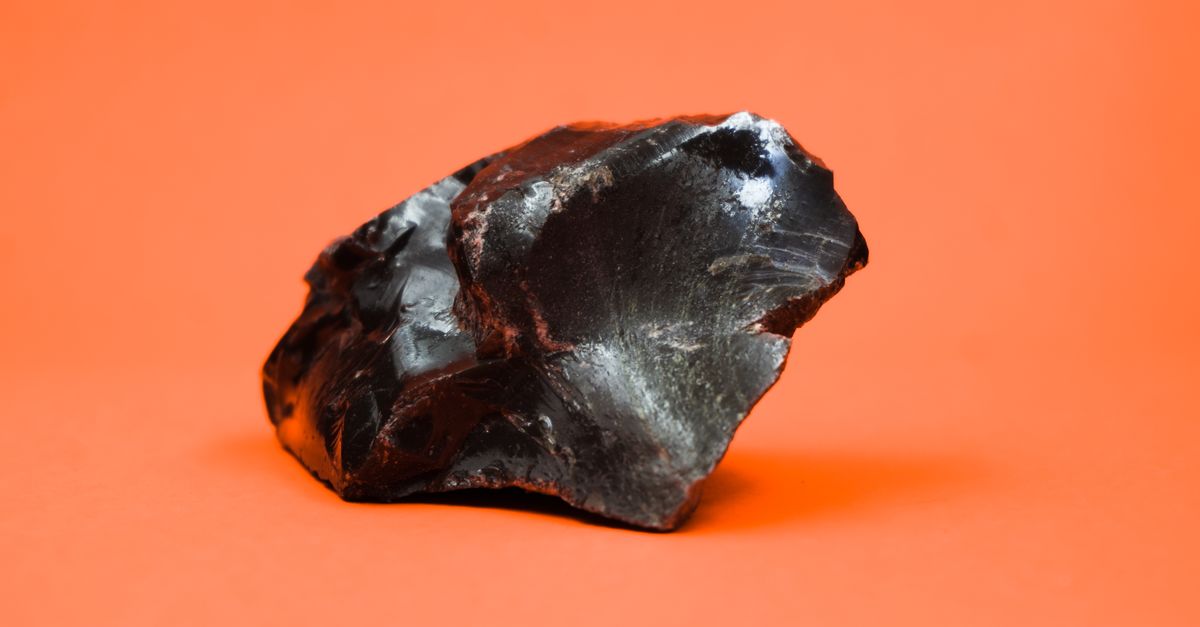 Close-up shot of a glossy obsidian stone with a sharp texture against a vibrant orange background.