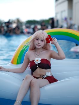 Woman in cosplay outfit enjoys a colorful rainbow float at a sunny pool event. Summer vibes.