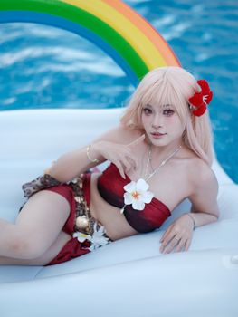 A mermaid-themed cosplay on a rainbow float in a tropical pool setting.