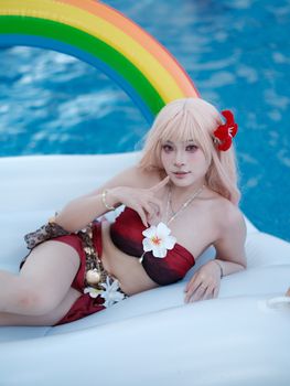 A cosplayer relaxes on a rainbow float in a pool, capturing a vibrant and summery atmosphere.