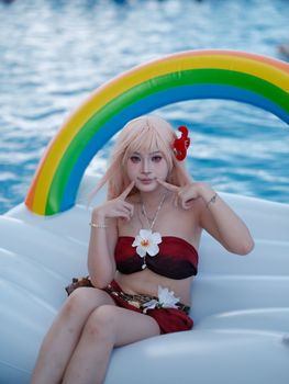 Woman in a bikini posing on a rainbow inflatable float in a pool.
