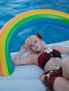 A woman in swimwear relaxes on a rainbow inflatable by a pool, exuding summer vibes.