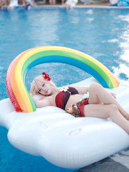 Woman in a swimsuit on a rainbow inflatable enjoying leisure time in a pool.