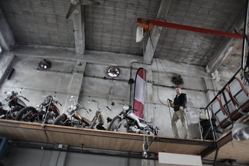 Serious mechanic standing near motorbikes parked together on special platform in garage