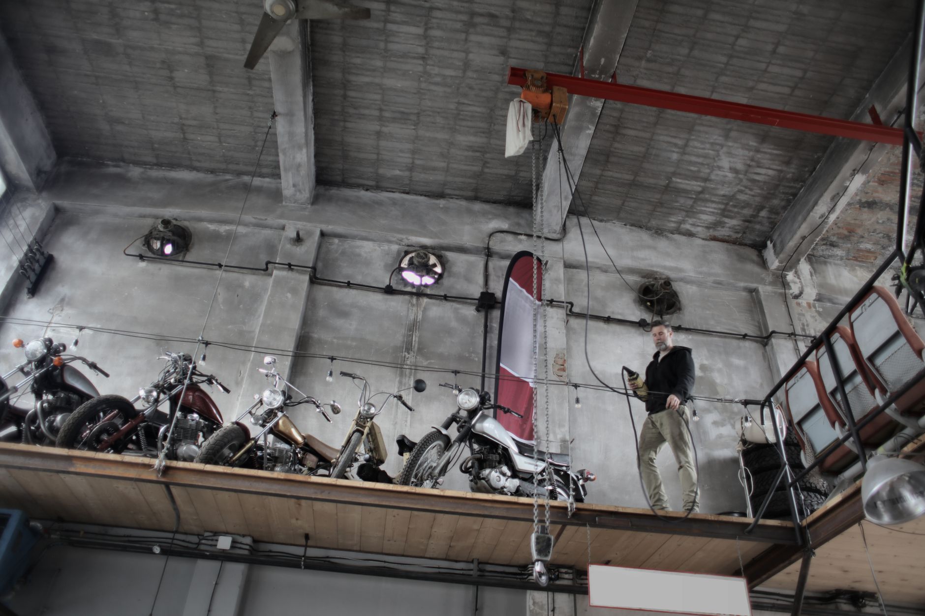 From below of bearded mechanic in casual outfit standing near motorcycles on special platform in garage and holding control panel in hand