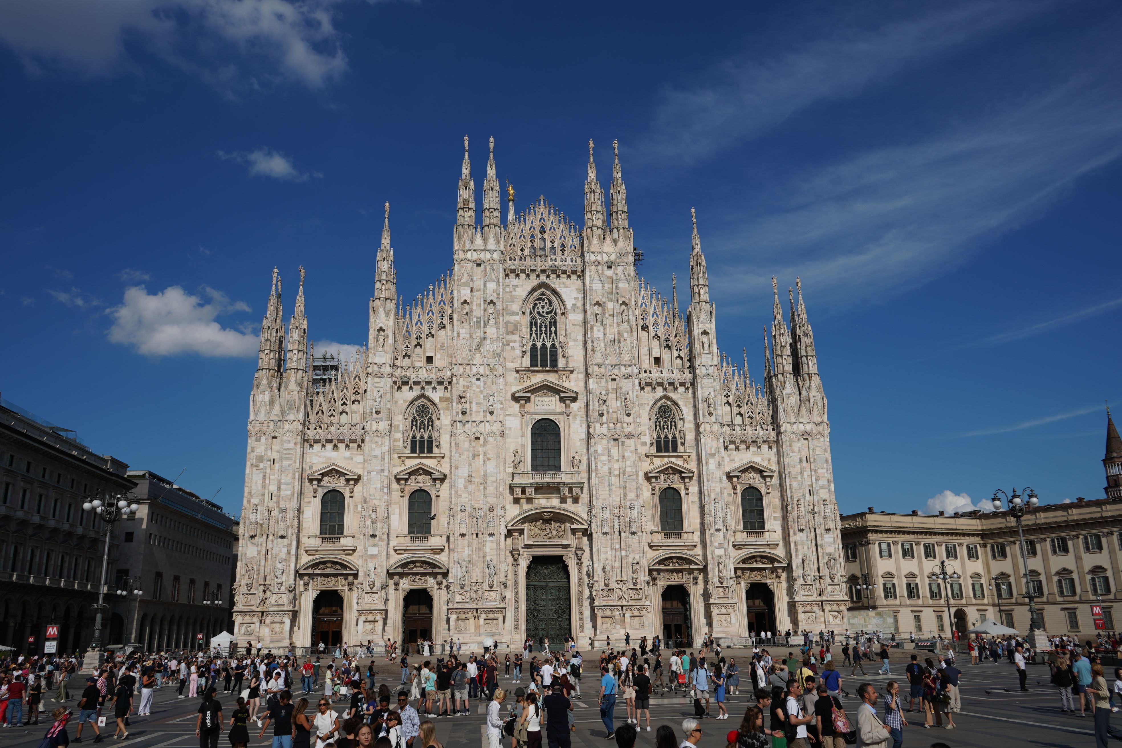 A striking view of Milan Cathedral with crowds in the sunny Piazza del Duomo.
