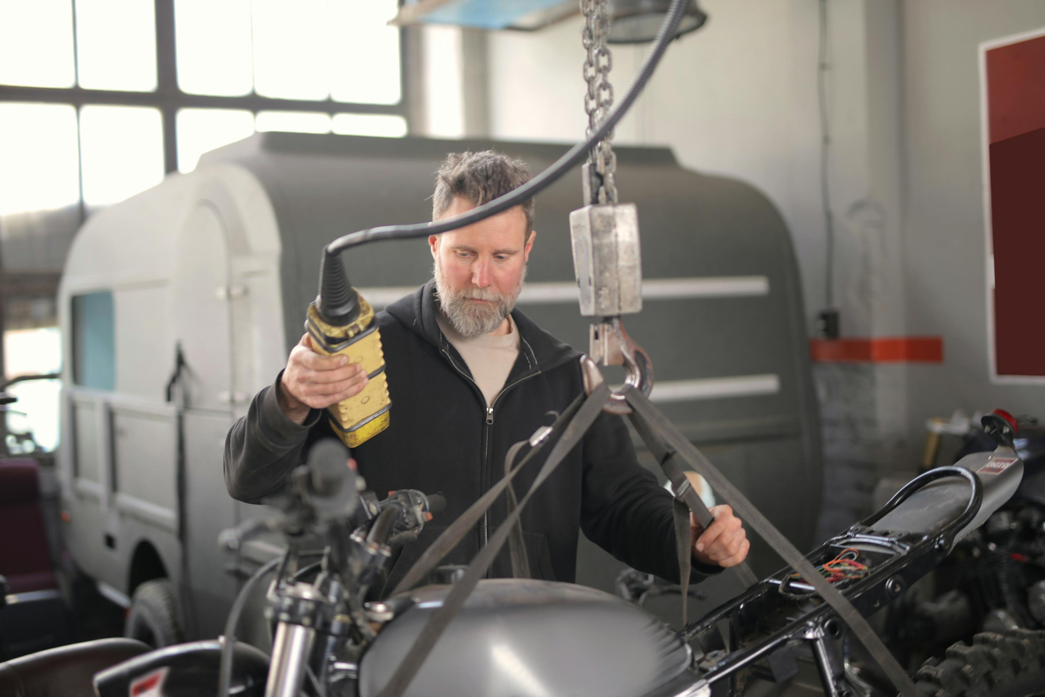 male mechanic using hydraulic crane in garage