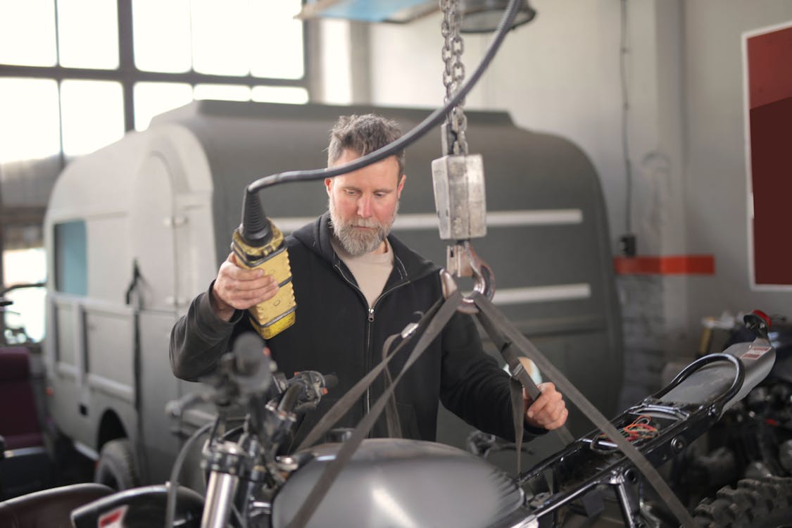 Free Male mechanic using hydraulic crane in garage Stock Photo