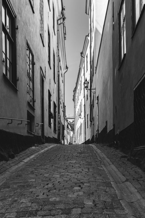 Free A monochrome view of a narrow cobblestone street flanked by historic European buildings. Stock Photo