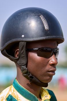 Close-up of an equestrian jockey wearing a helmet and sunglasses outdoors.