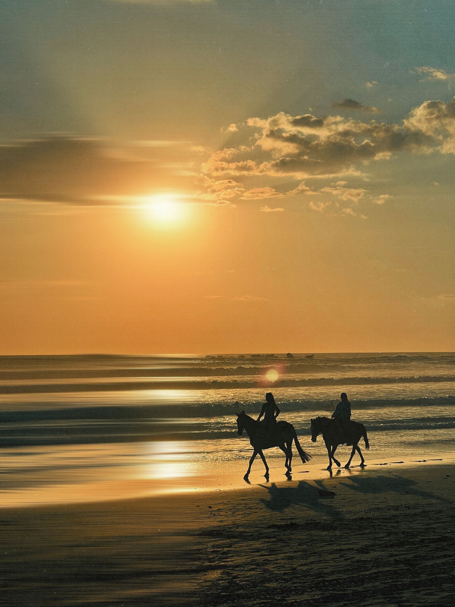 Two people riding horses on a Costa Rican beach at sunset